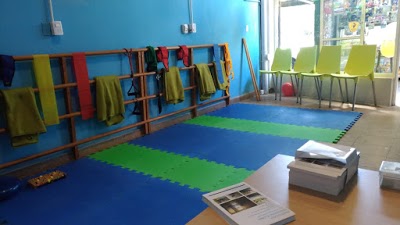 Modern bright physical therapy and kinesiology clinic treatment room in Buenos Aires, clean clinical physiotherapy interior, treatment table with fresh towels, rehabilitation equipment, warm natural light, wooden accents, indoor plant, calming trustworthy atmosphere, high-end medical interior photography, 8k resolution.
